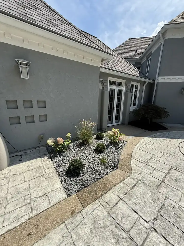 Decorative rock bed with plantings beside a stamped concrete patio, by J’s Design